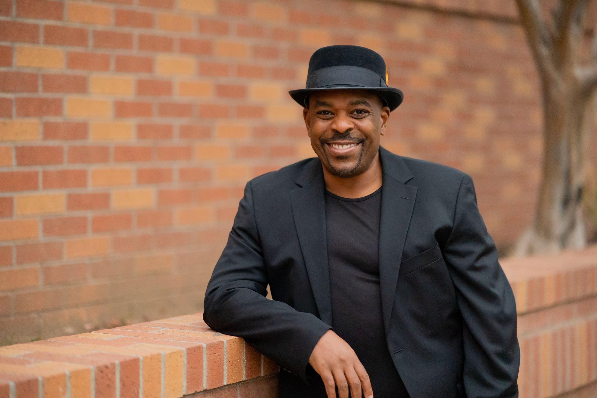 Woman in green coat leaning on brick wall, smiling.