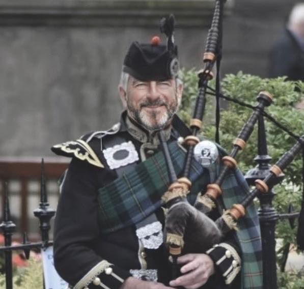 Woman in green coat leaning on brick wall, smiling.