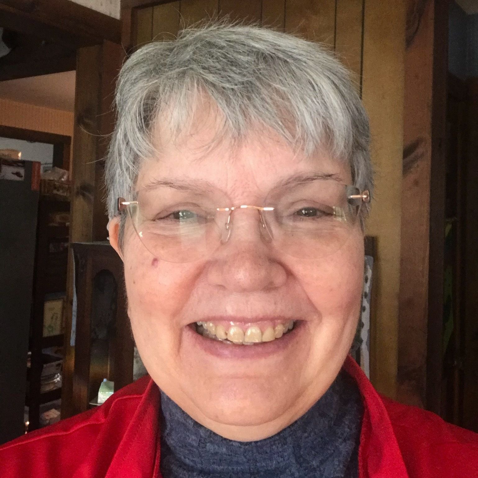 A woman wearing glasses and a red jacket is smiling for the camera.