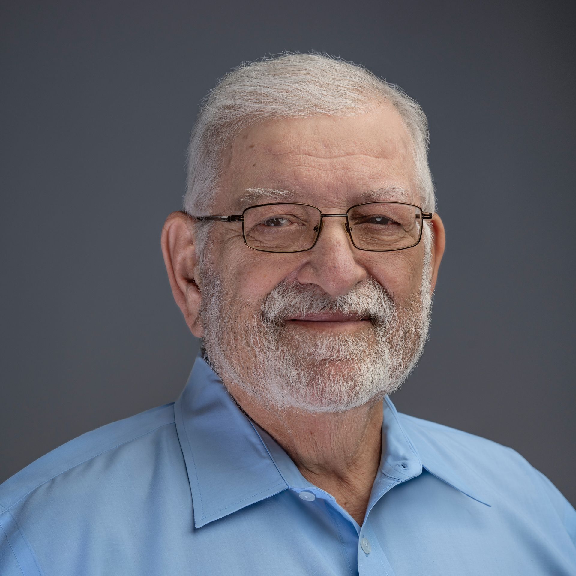 A man with a beard and glasses is wearing a blue shirt.