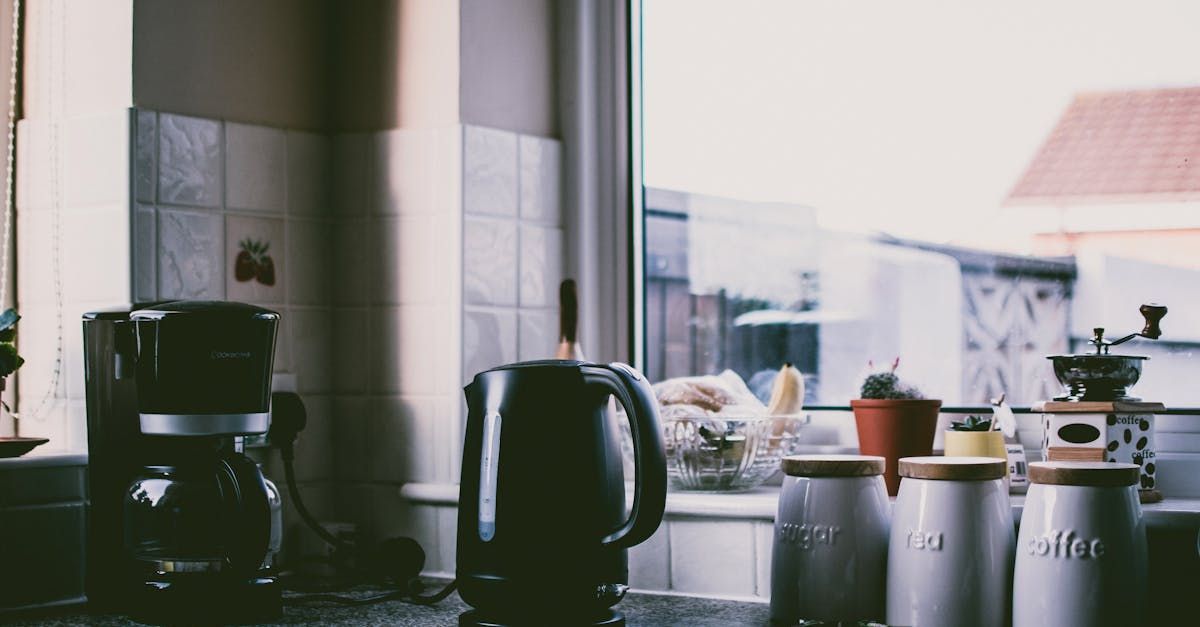 A kitchen counter with a coffee maker , kettle , and coffee canisters.
