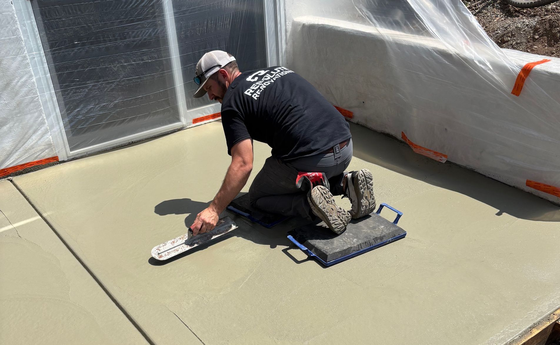 Man kneeling, smoothing wet concrete on patio with a trowel.