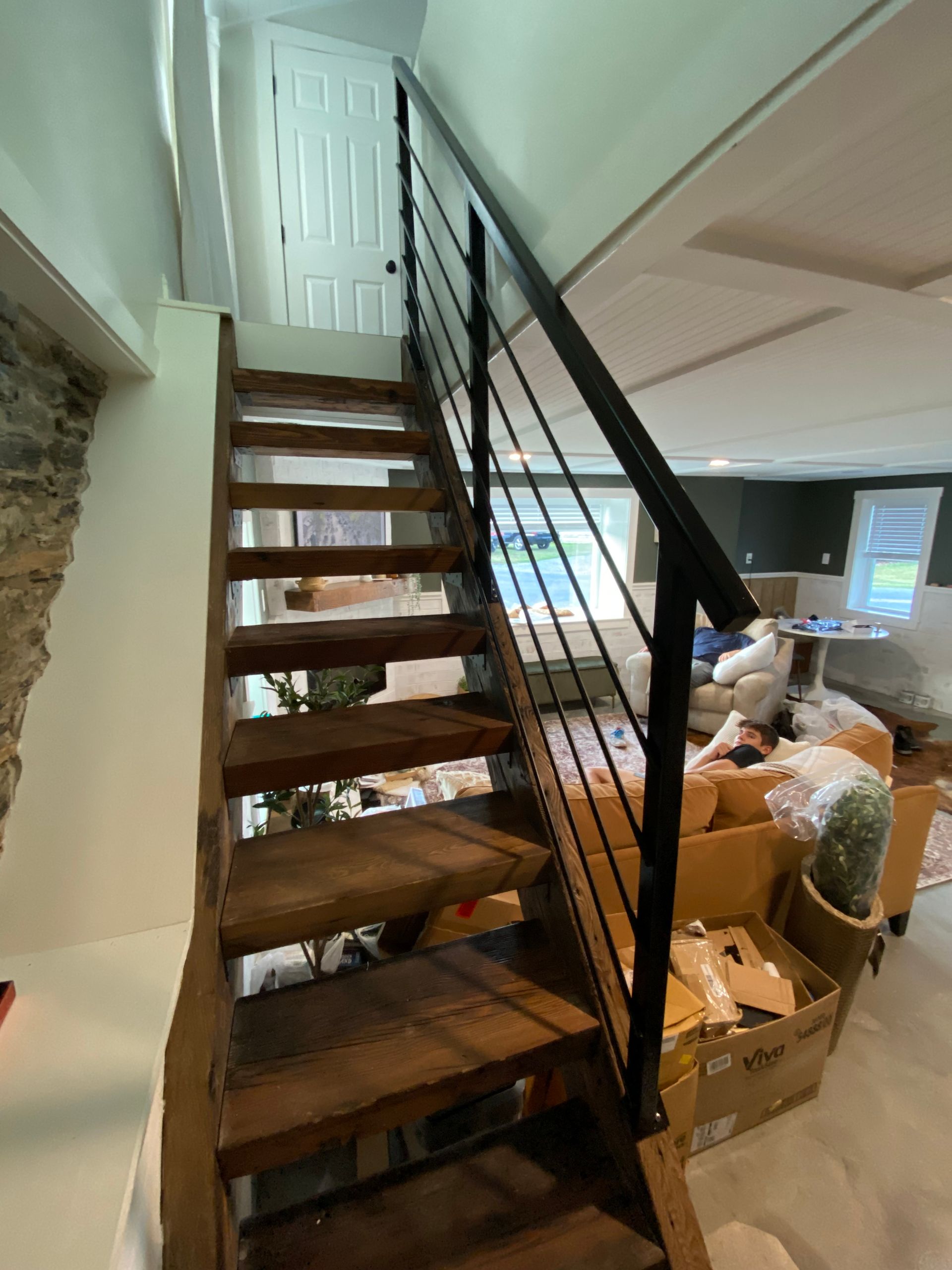Wooden staircase with black metal railing, leading to a white door. Interior view.