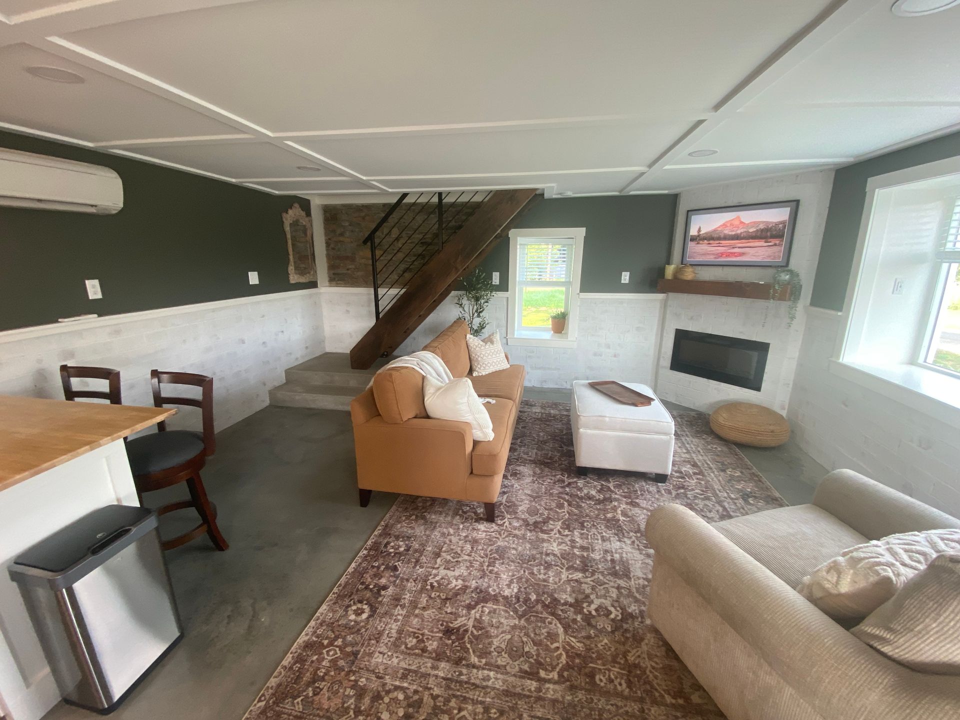 Living room with tan furniture, brick stairs, fireplace, rug, and green accent wall.