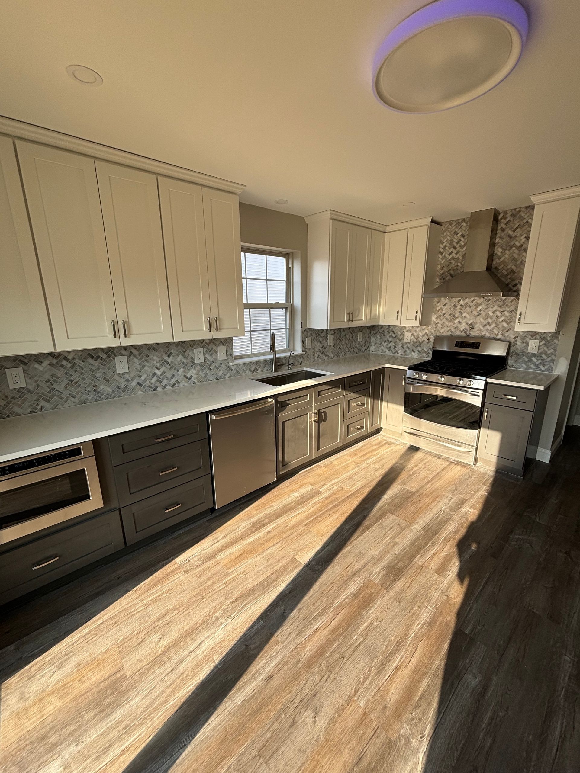 Modern kitchen with white upper cabinets, gray lower cabinets, and stainless steel appliances; wood-look flooring.