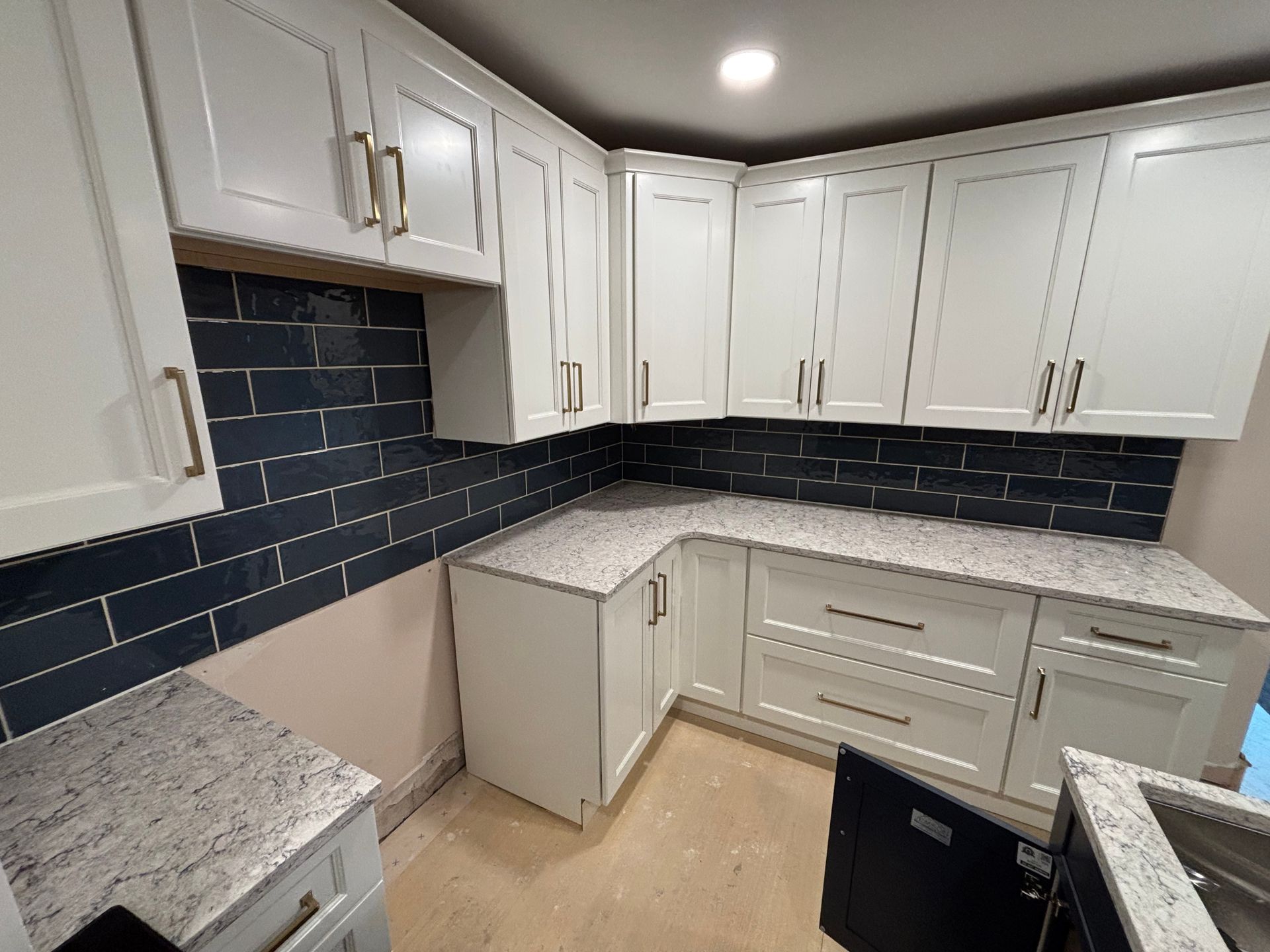 White kitchen cabinets with granite countertops and dark blue subway tile backsplash.