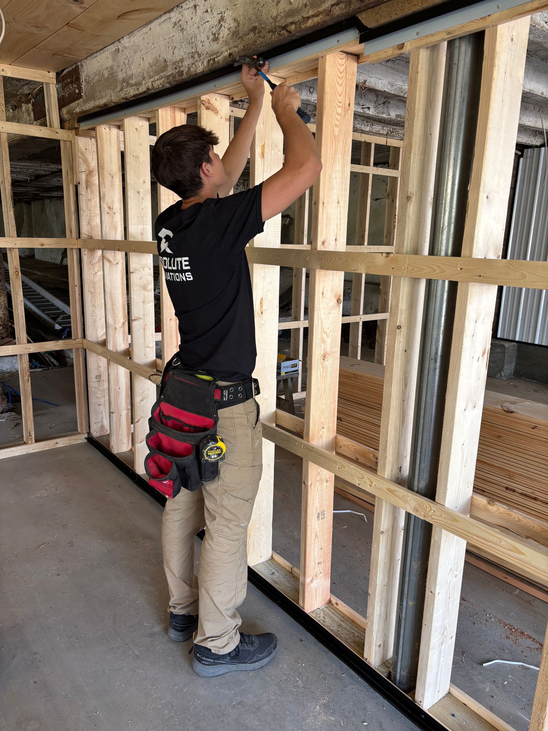 Construction worker installing something on a wooden frame wall, inside a building.