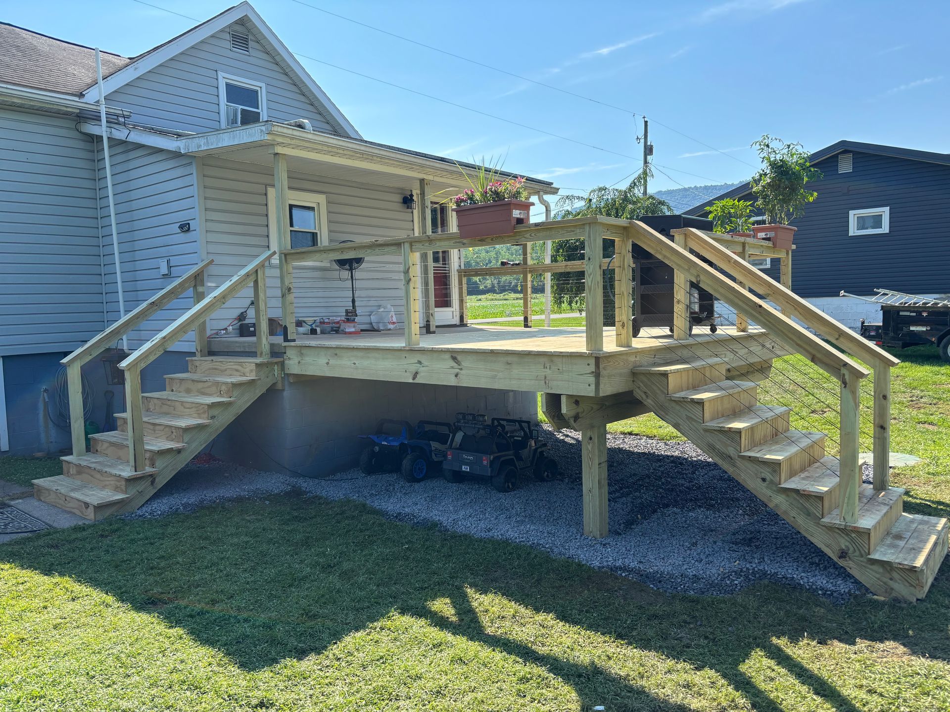 Wooden deck with stairs attached to a house with a porch, set in a grassy yard.