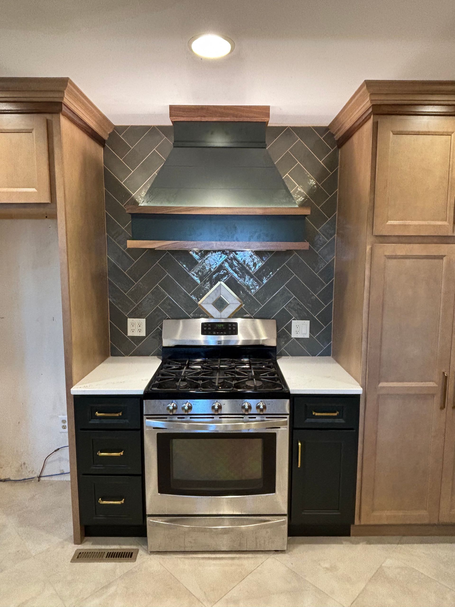 Kitchen with stainless steel stove, gray backsplash, dark green cabinets, light wood cabinets.