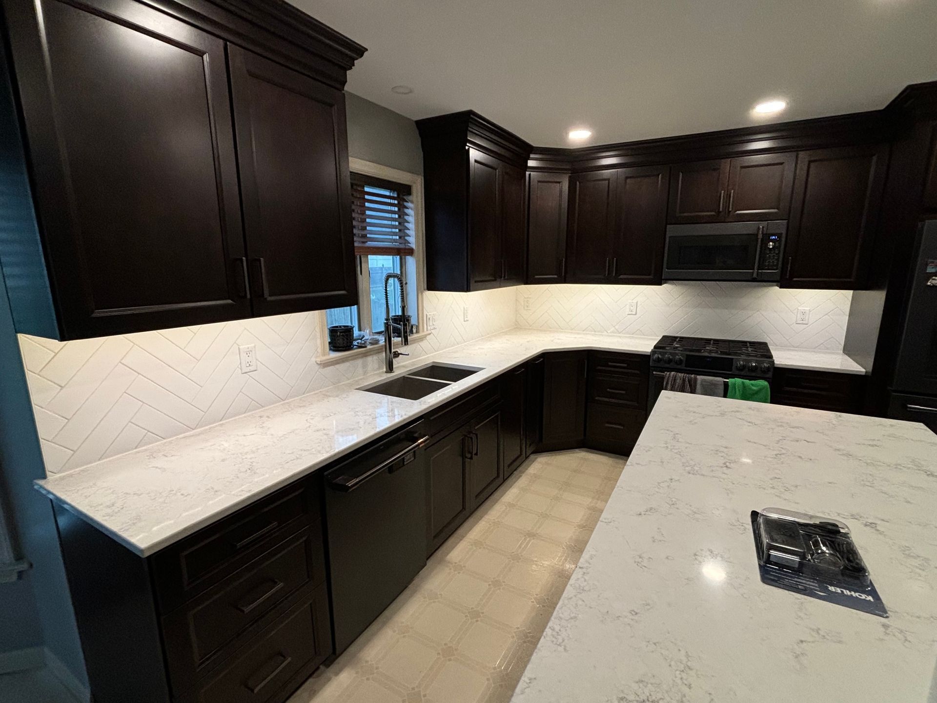 Dark wood kitchen cabinets with white countertops and a patterned backsplash.