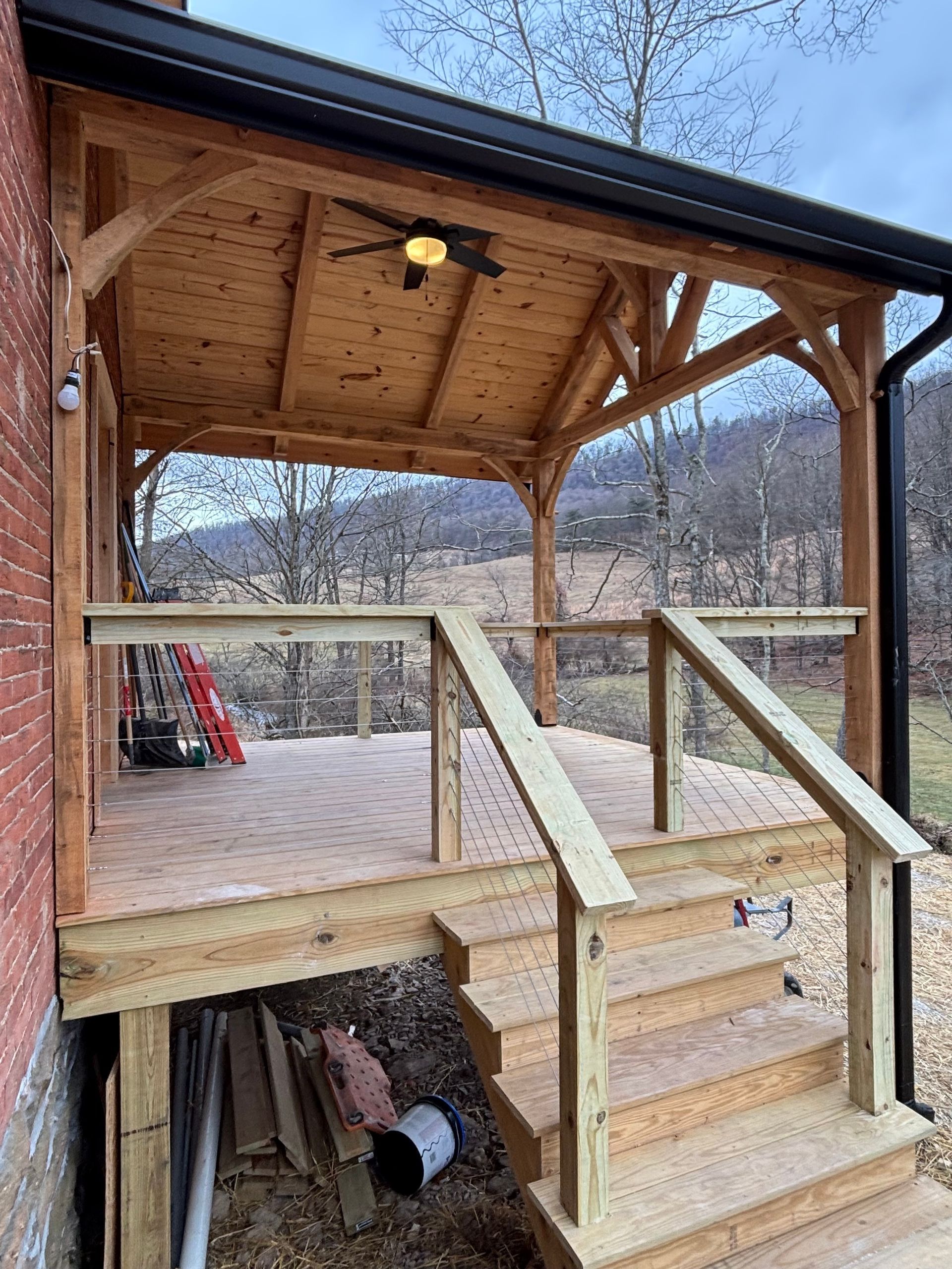 Wooden deck and covered porch with a railing and steps, built onto a red brick building.