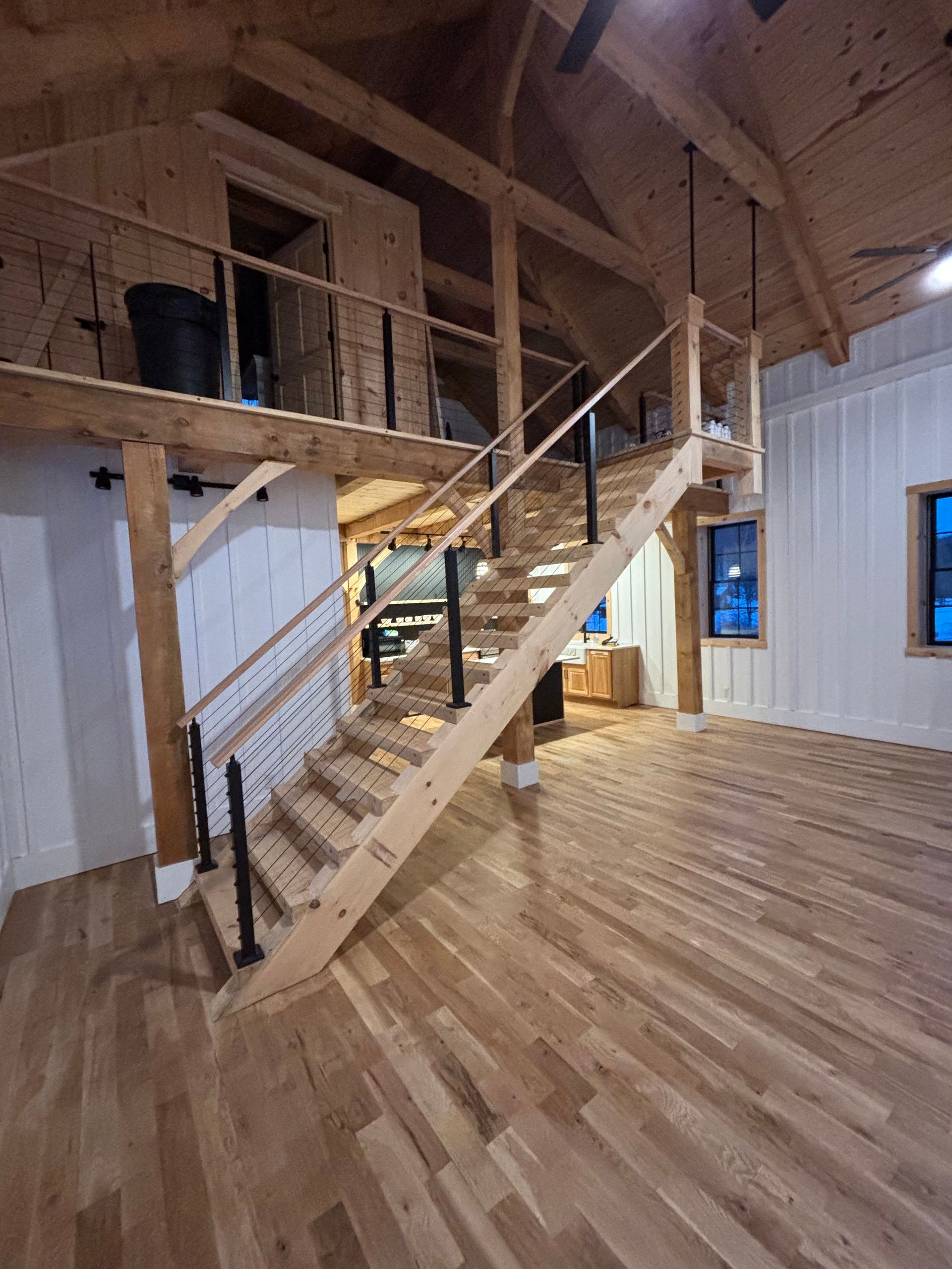 Wooden staircase leads to a loft in a light-filled room with wood floors and white walls.