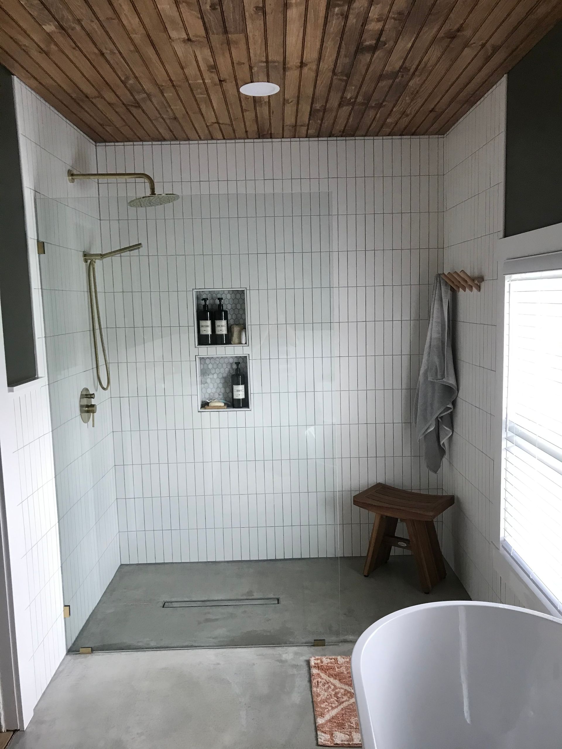Bathroom with white tiled shower, wood ceiling, bench, and soaking tub.