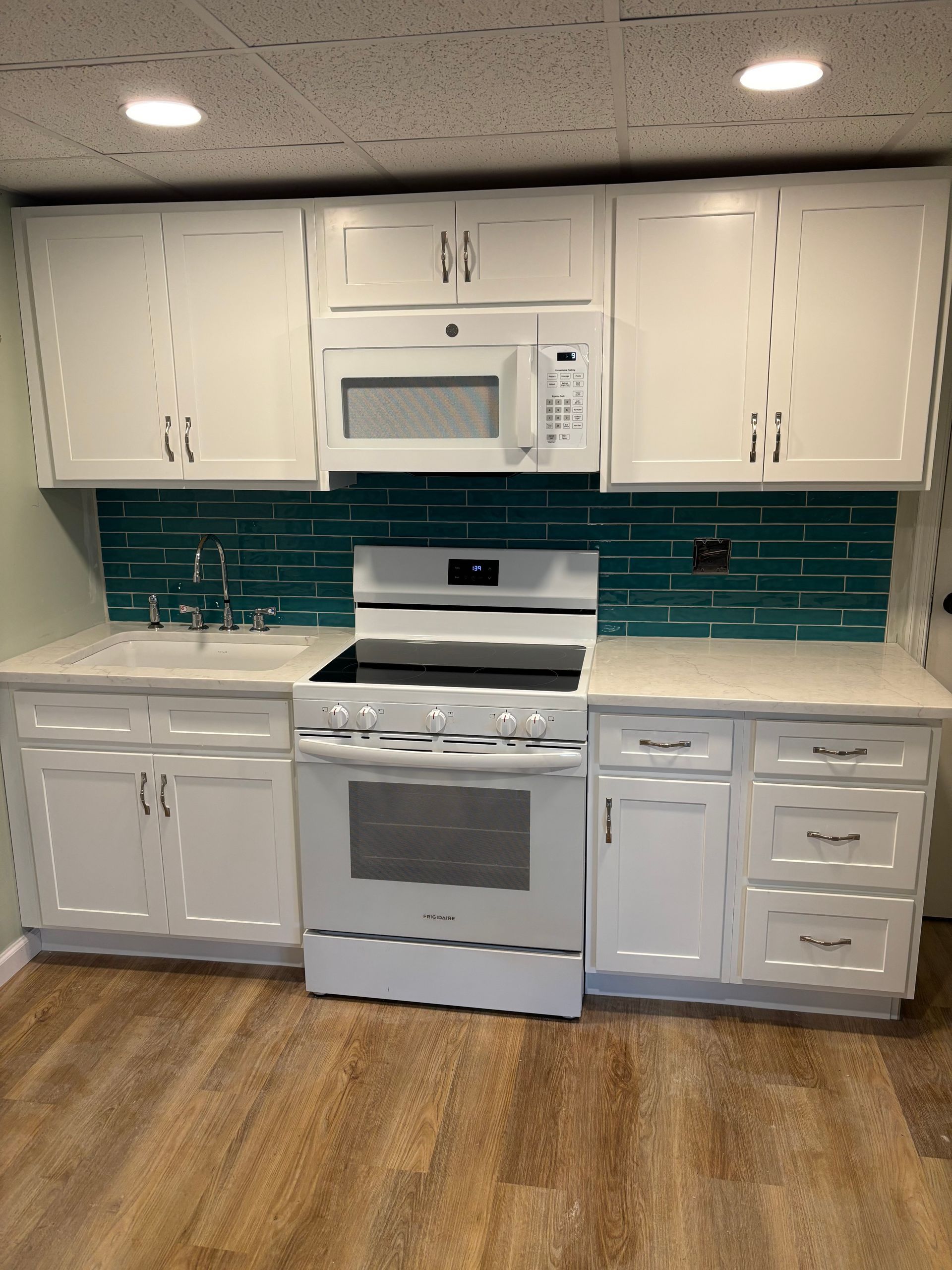 White kitchen cabinets with teal backsplash and white appliances on wood floor.