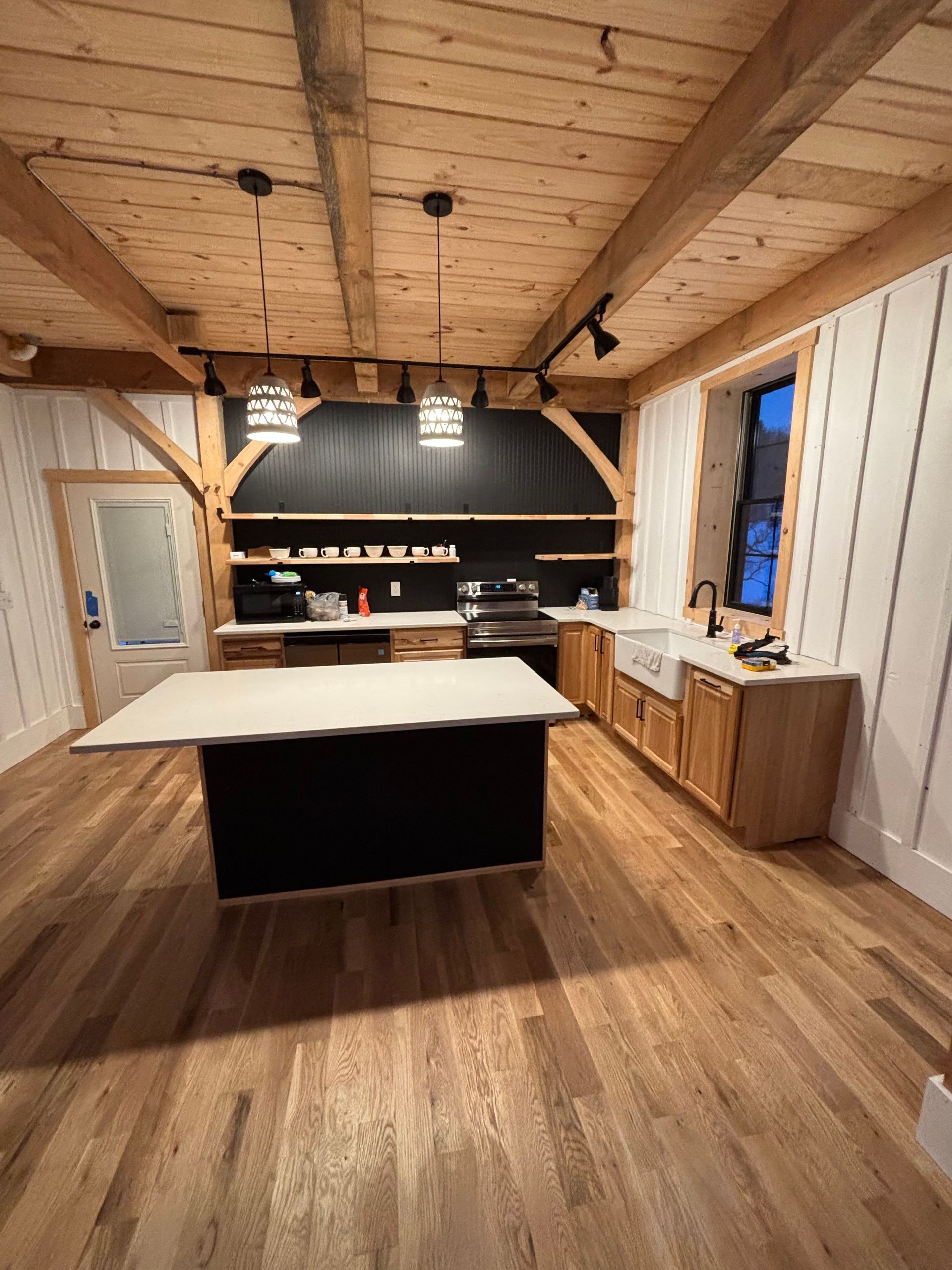 Kitchen with wood floors, white walls, black island, and exposed beams.
