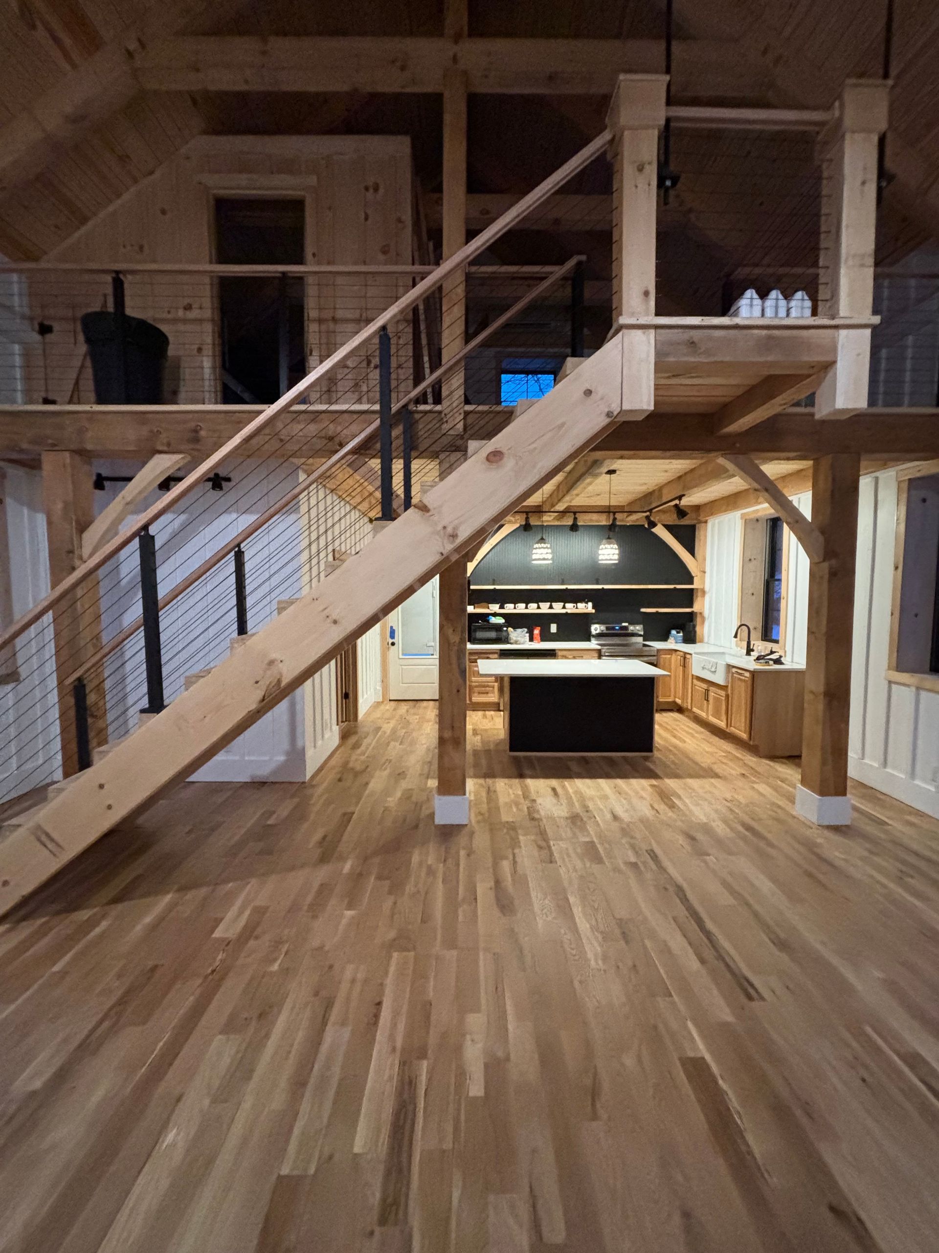 Spacious interior with wooden beams, staircase, and second-floor loft. Kitchen in the background.