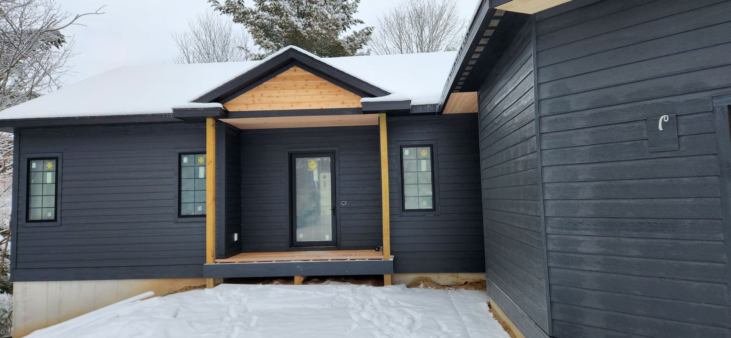 A black house with a porch in the snow.