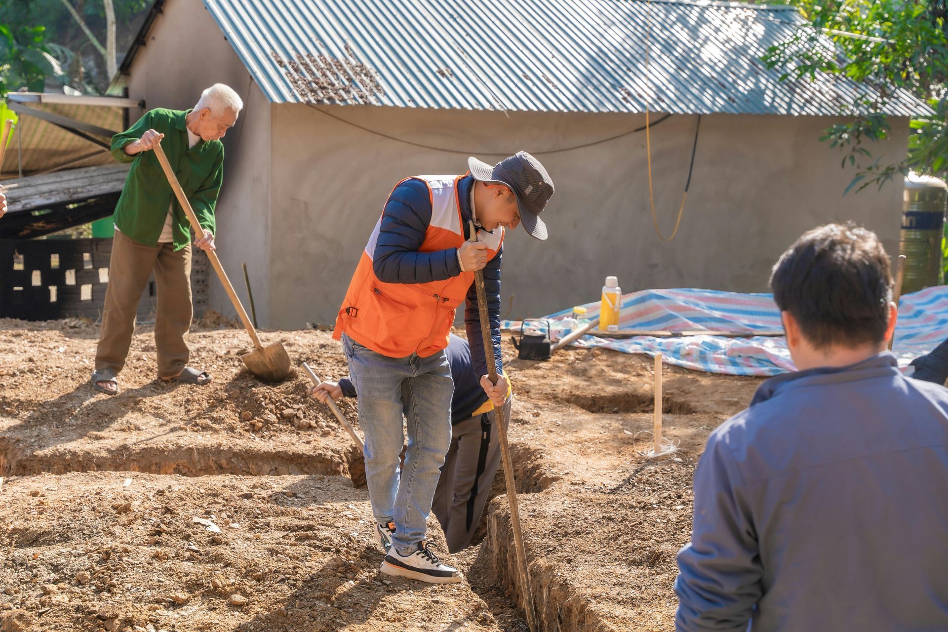 Men digging in dirt near a small building with a tin roof.