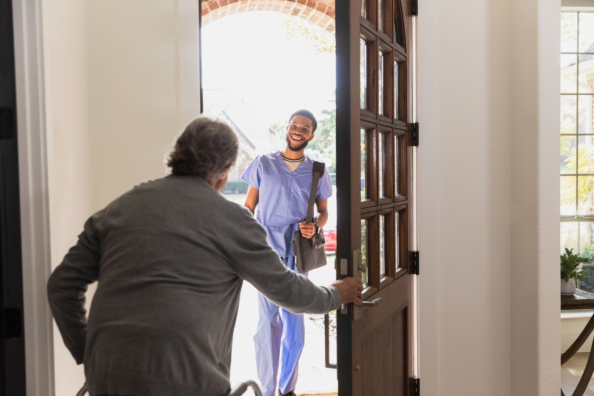 Older person opens door for smiling healthcare worker.