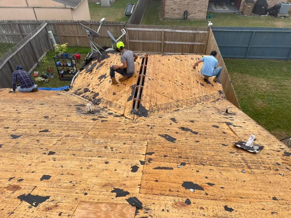 Roofers removing old shingles from a roof, with wooden decking visible; daytime.