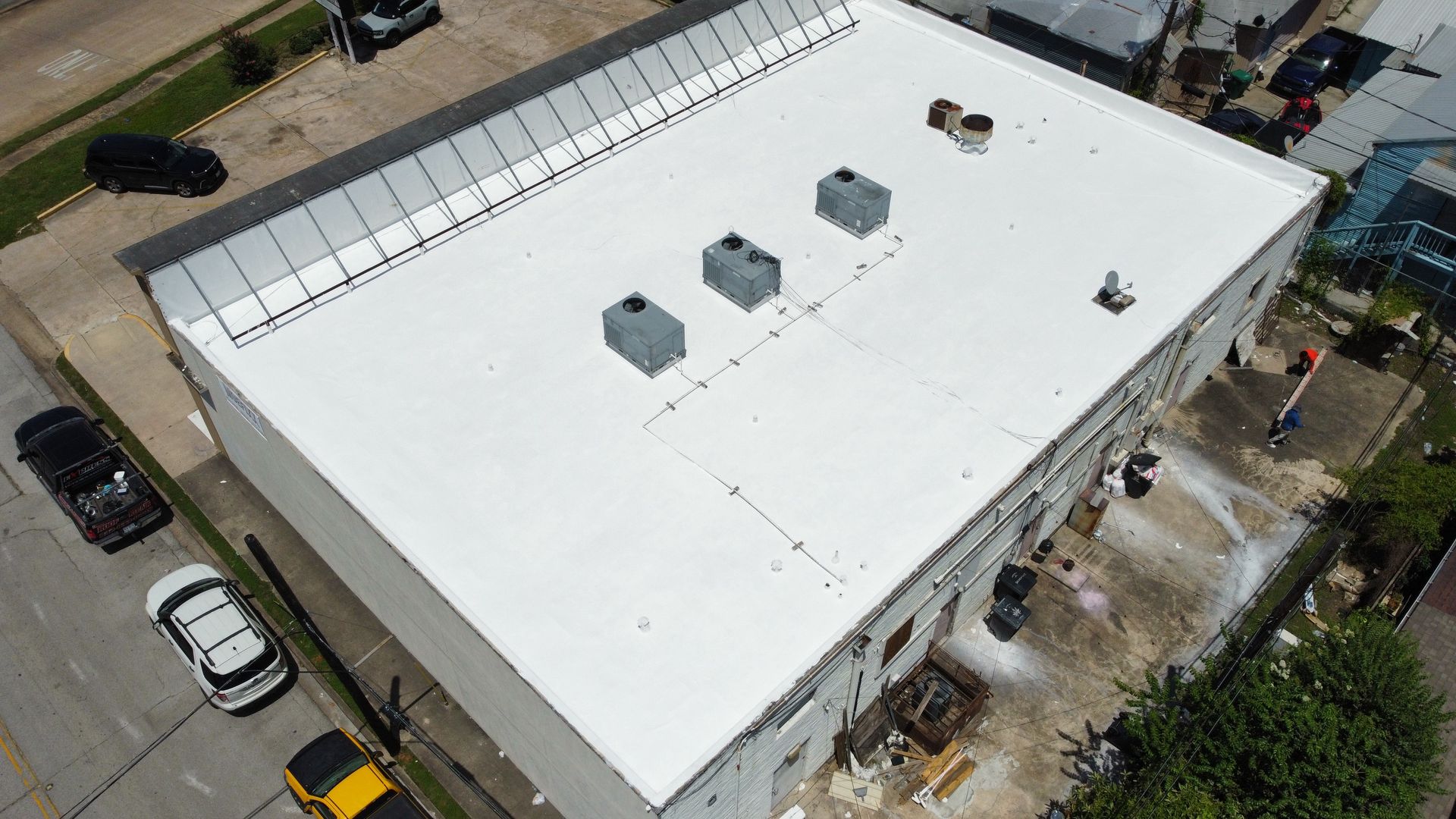 Aerial view of a white commercial building with air conditioning units on the roof and cars parked nearby.