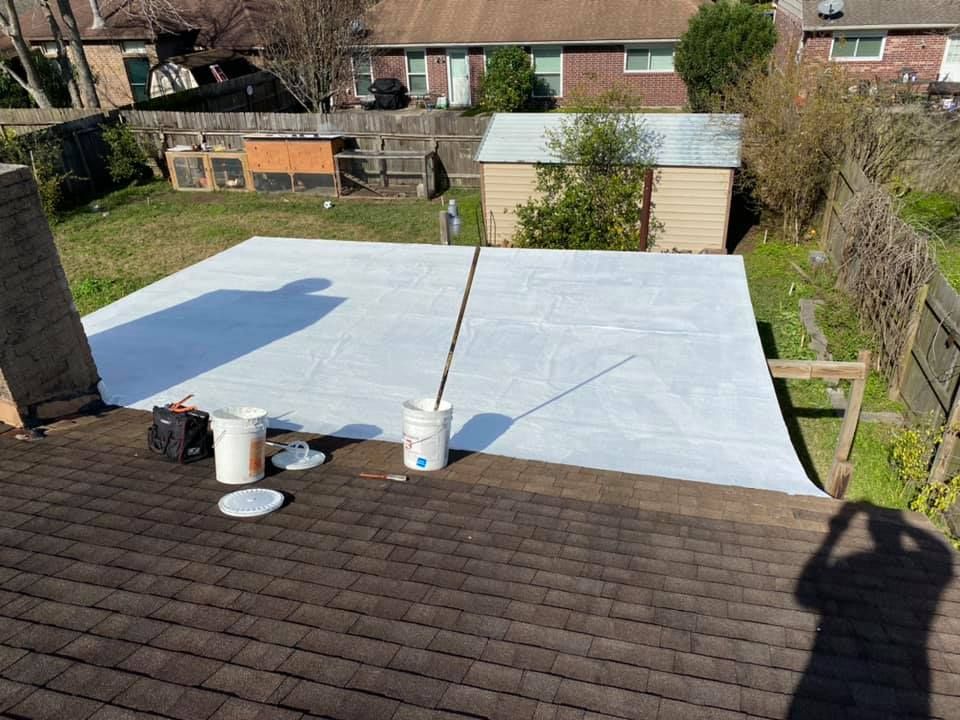 White tarp covers a roof. Buckets, tools, and a shadow are present. Backyard in the background.