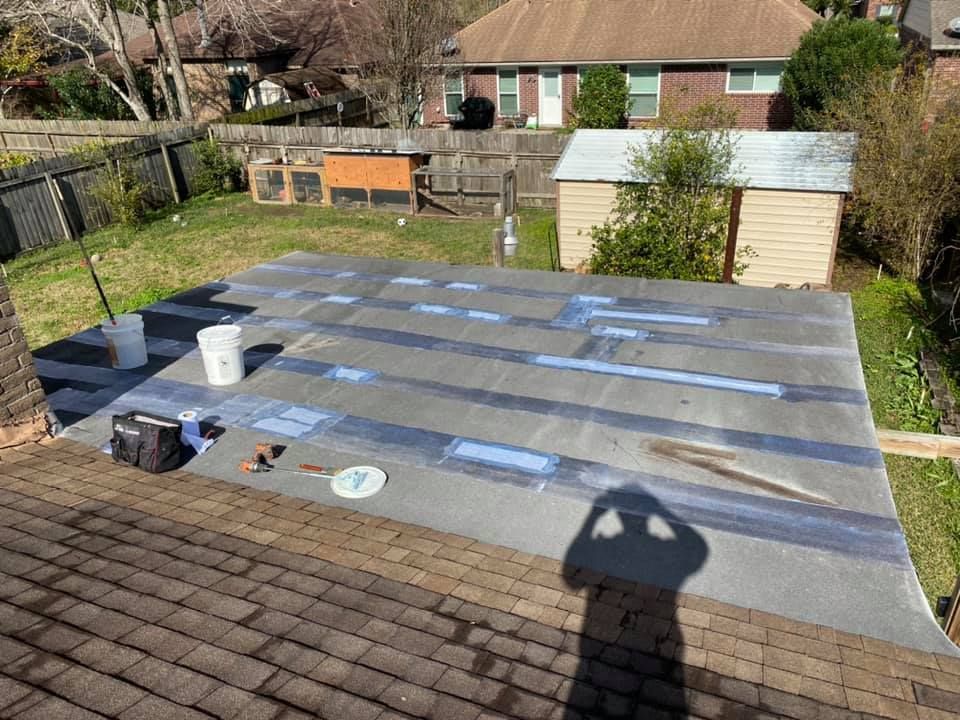 A person repairing a flat roof. Gray material with blue tape. Backyard with shed, lawn, and fence.