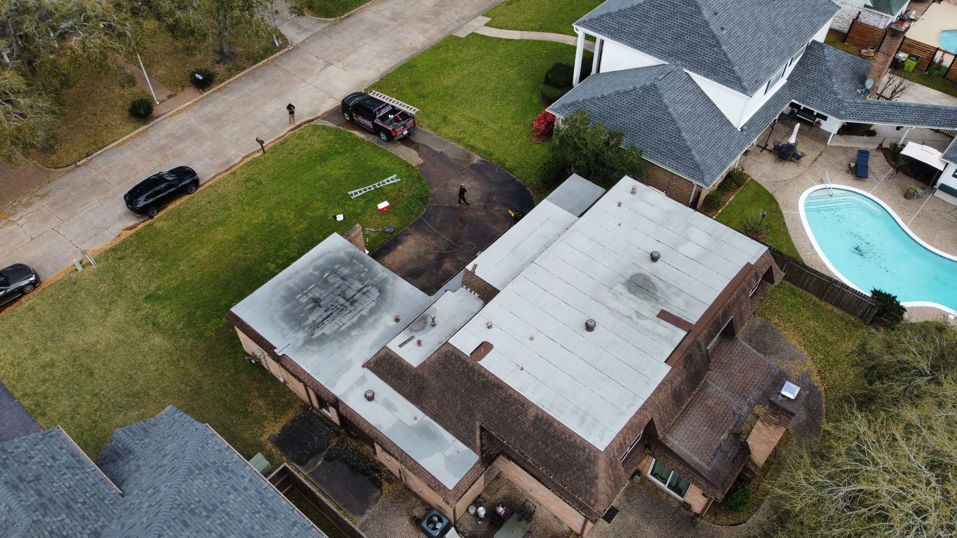 Aerial view of houses with a pool in a neighborhood; cars parked on streets and a driveway.
