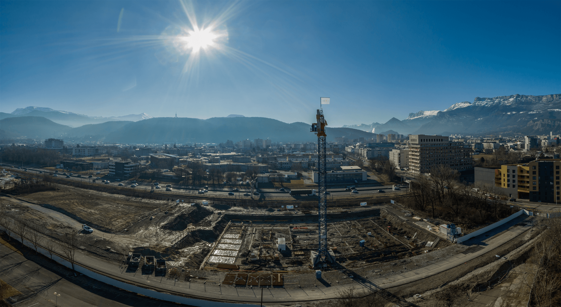 Une vue aérienne d'un chantier de construction dans une ville avec des montagnes en arrière-plan.