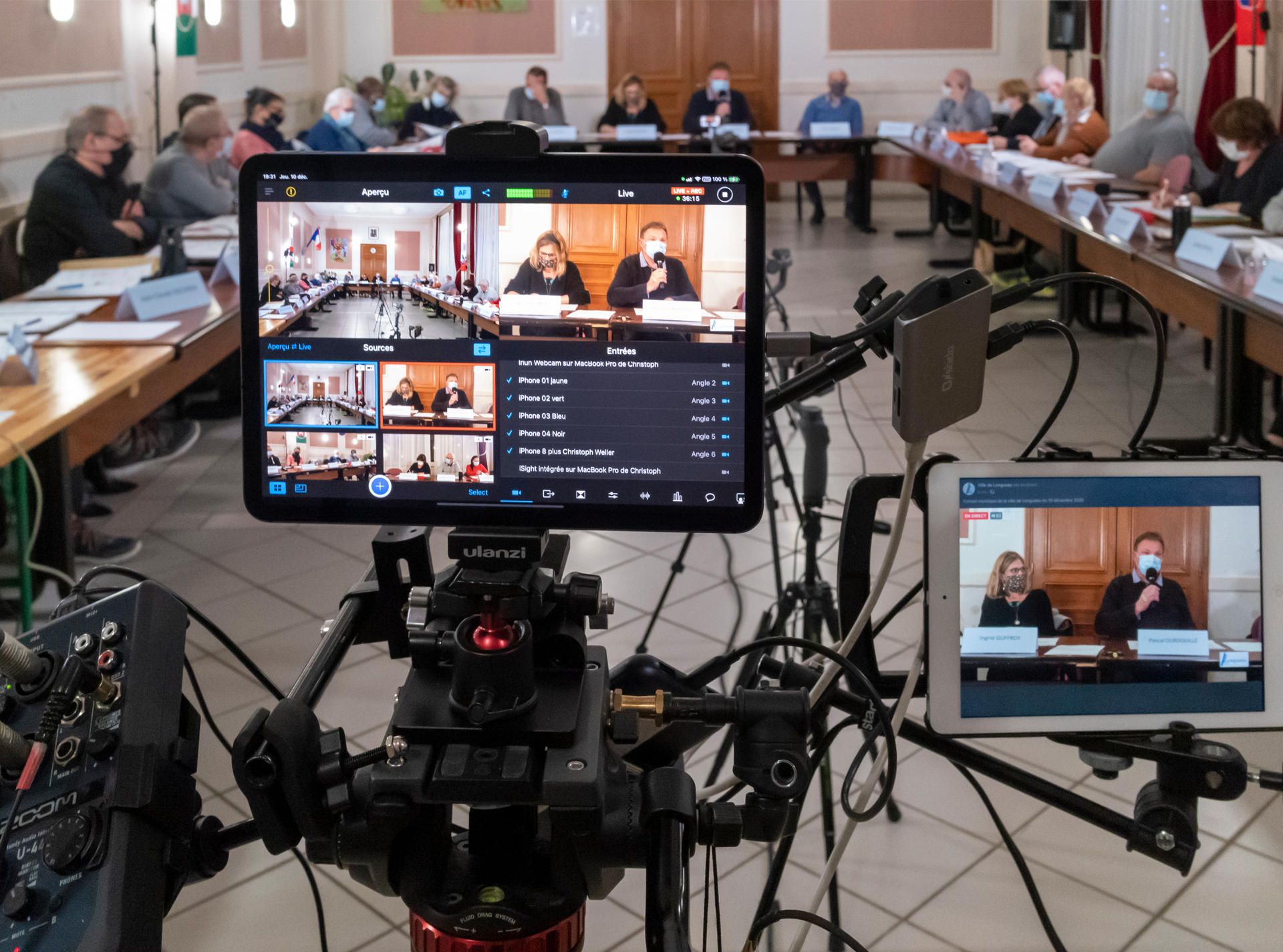 Un groupe de personnes est assis à de longues tables devant une caméra vidéo.