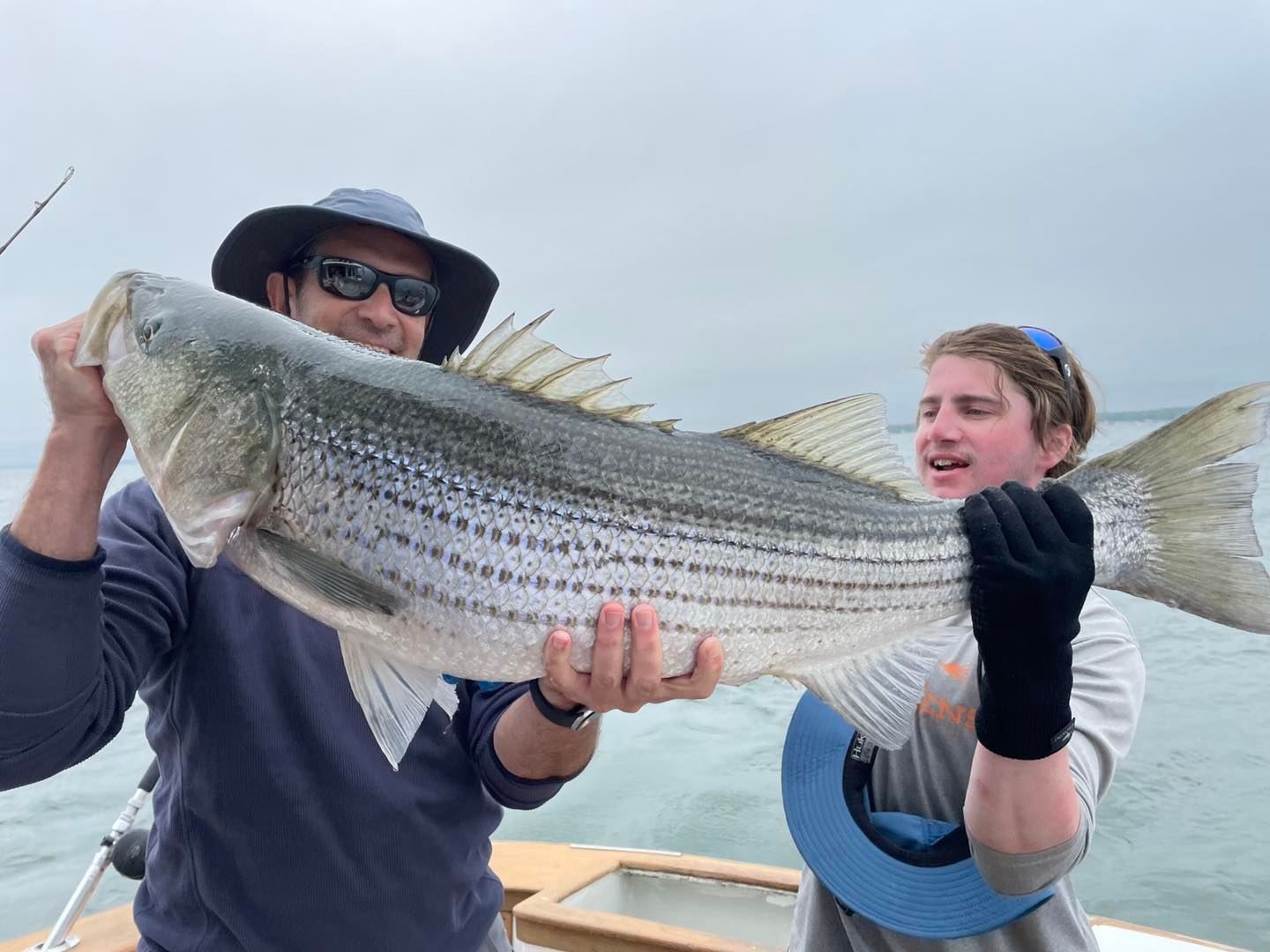 Two people holding a large striped fish on a boat, with open water in the background.