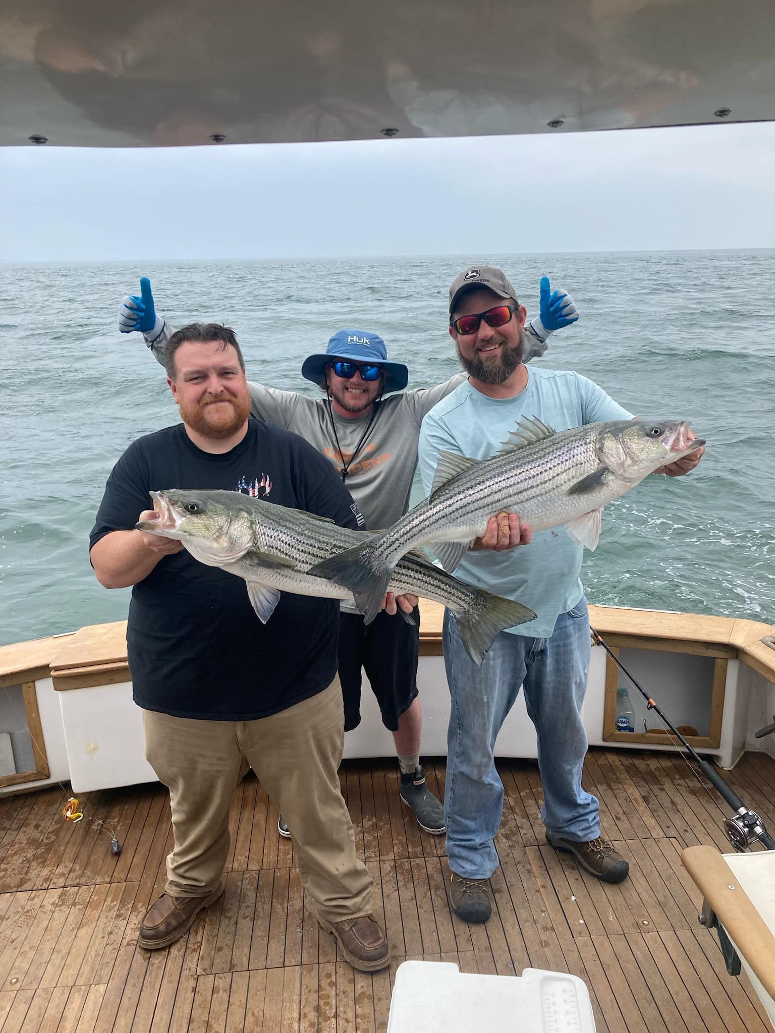 Three anglers on a boat hold up a large striped fish at sea, smiling
