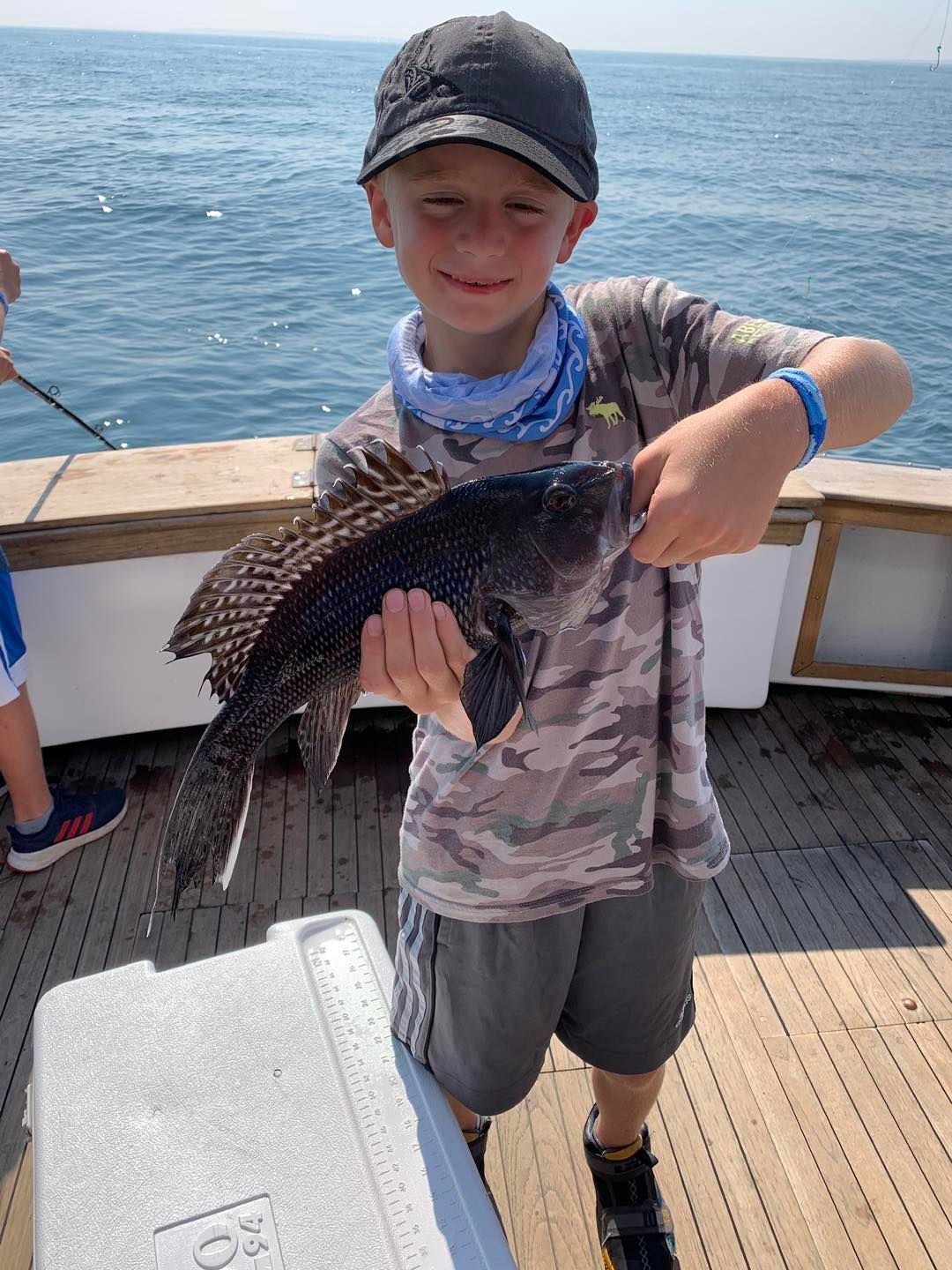 Boy on a boat holding a large fish, with the ocean in the background.