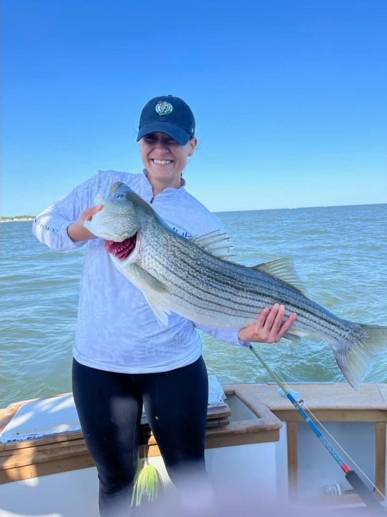 Person on a boat holding a large striped fish on open water under a clear blue sky