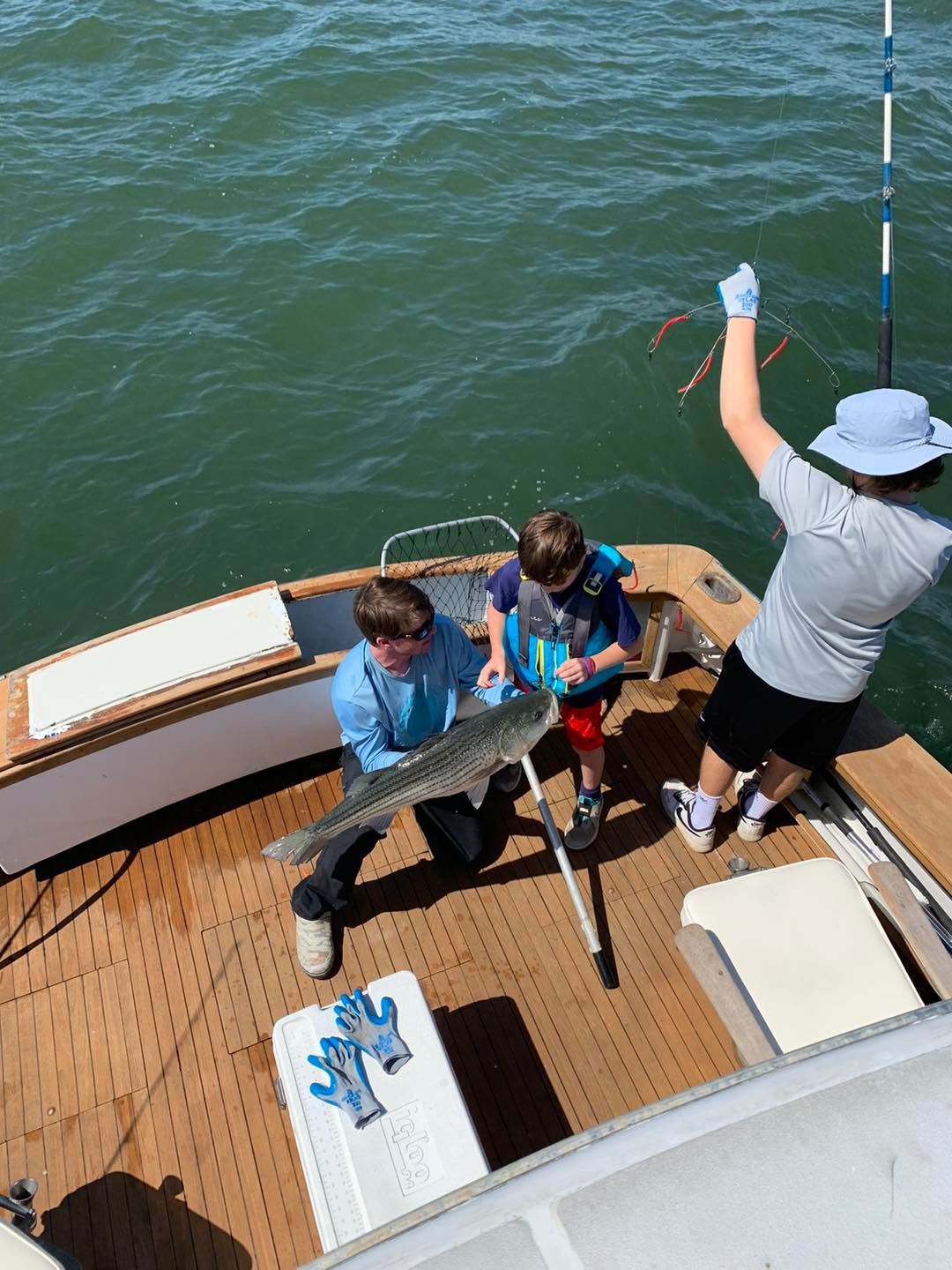 People fishing on a boat deck over green water, one person holding up a fish.