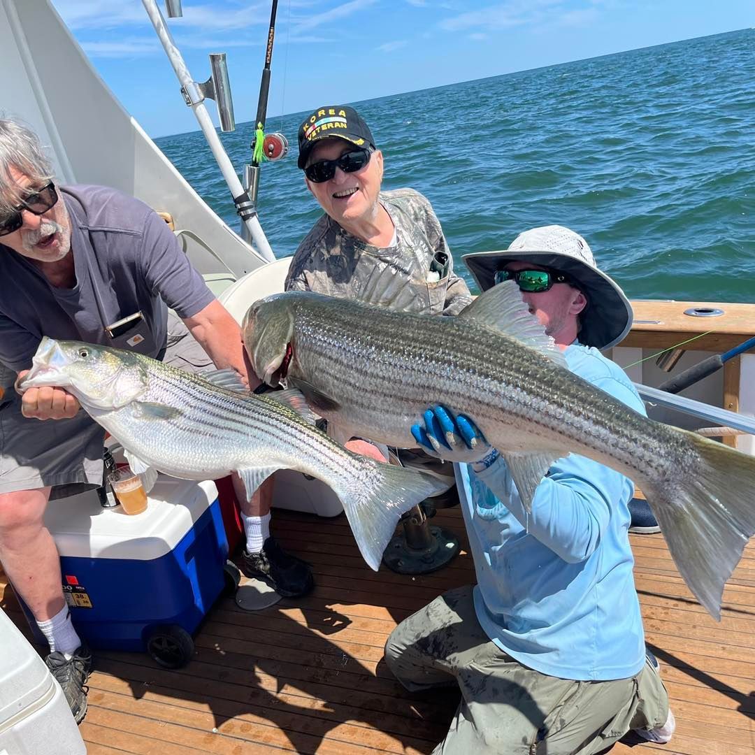 People on a boat holding two large striped fish on a sunny day at sea