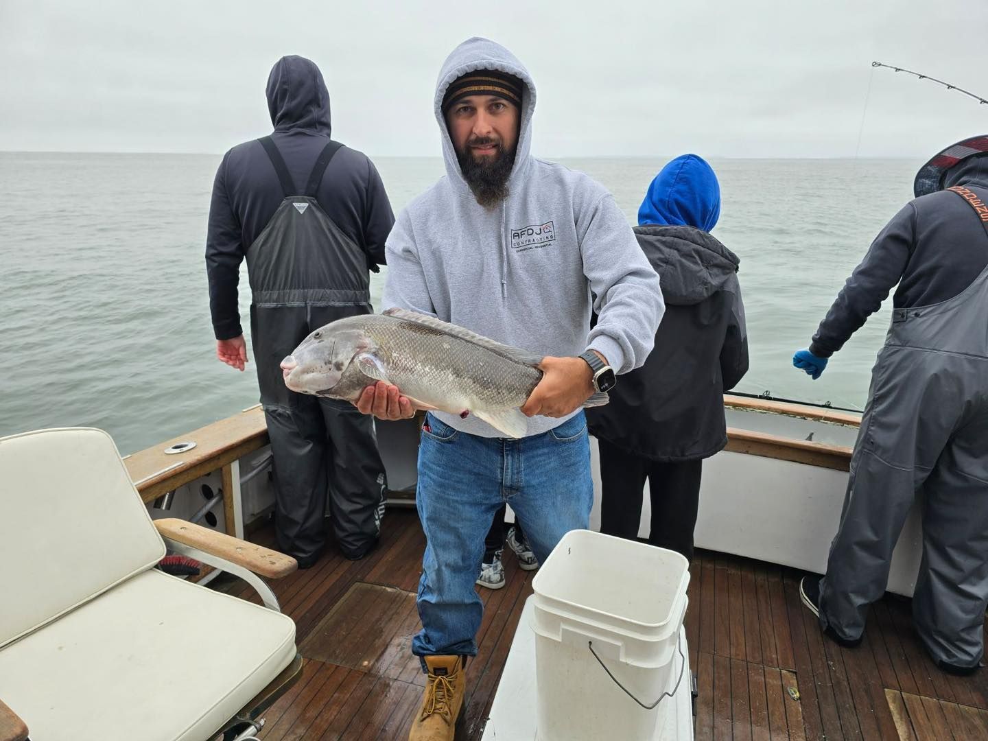 Man holding a large fish on a boat deck with three others on a foggy sea.