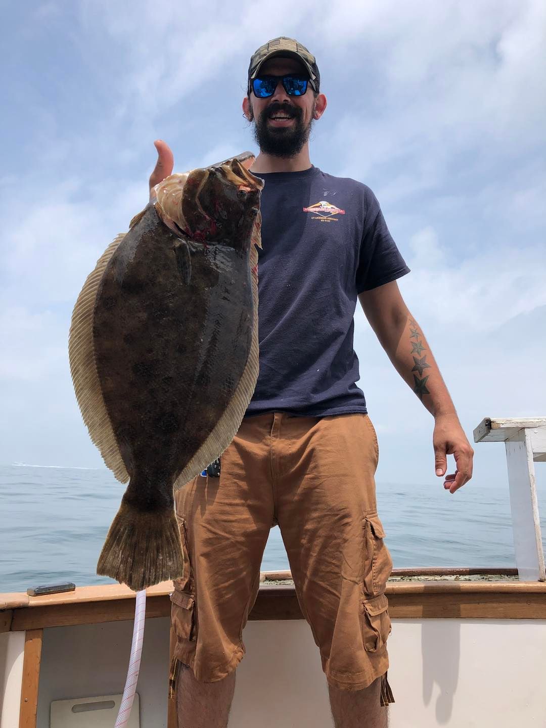 Man holding a large fish on a boat deck under a cloudy sky.