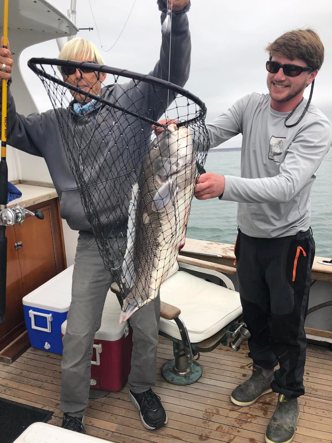 Two people on a boat hold up a large fish in a landing net after a catch