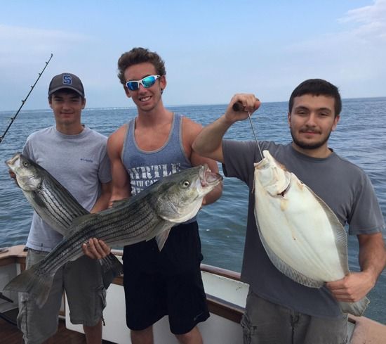 Three individuals holding fish while on a boat out at sea.