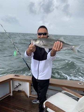 Person on a boat holding a striped fish, with fishing rods and choppy water in the background