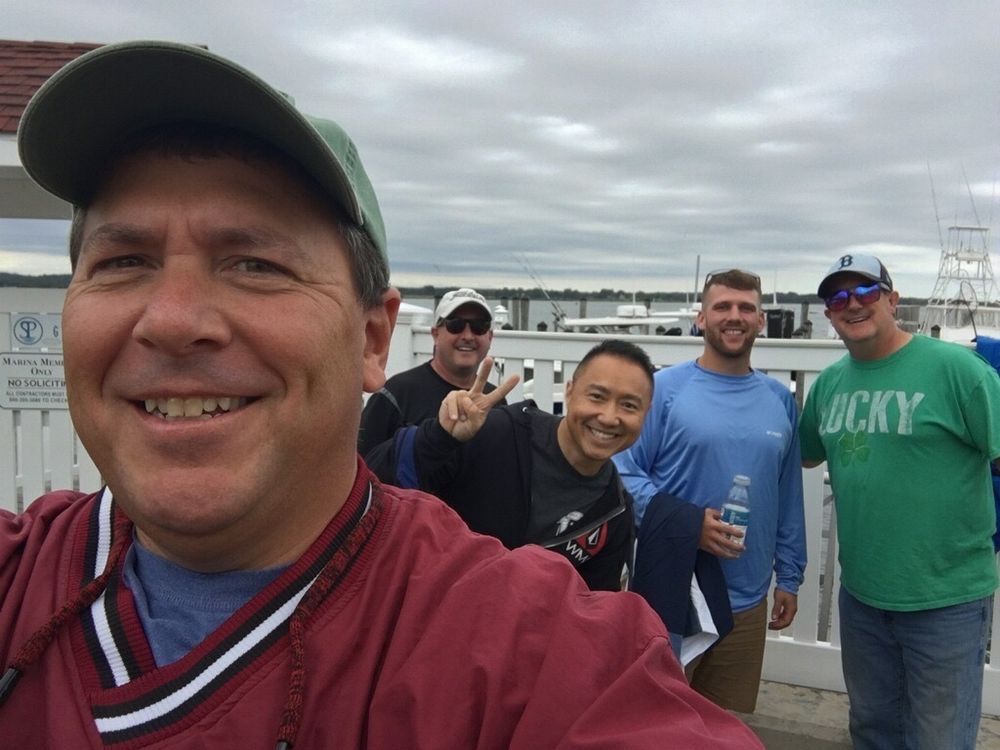 Five smiling friends taking a selfie on a bridge with cloudy skies in the background