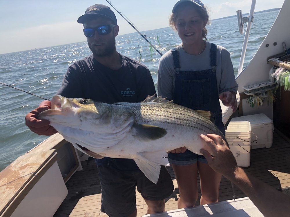 Two people on a boat holding a large striped fish over the ocean