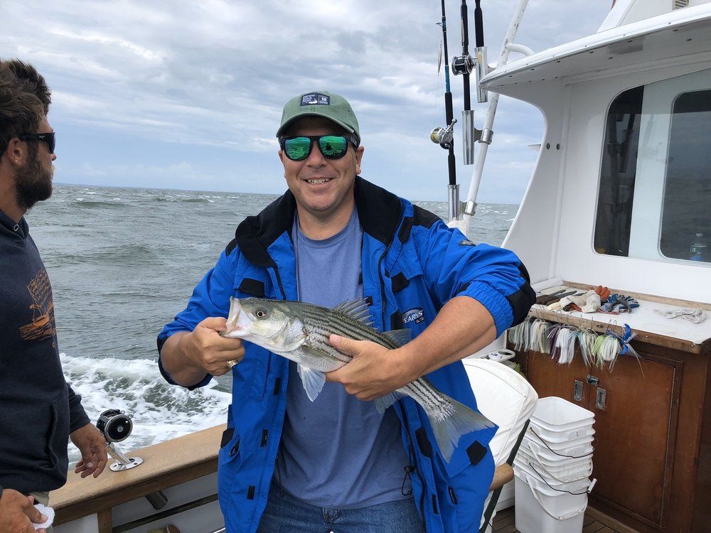 Smiling angler in blue jacket and green cap holds a fish on a boat at sea