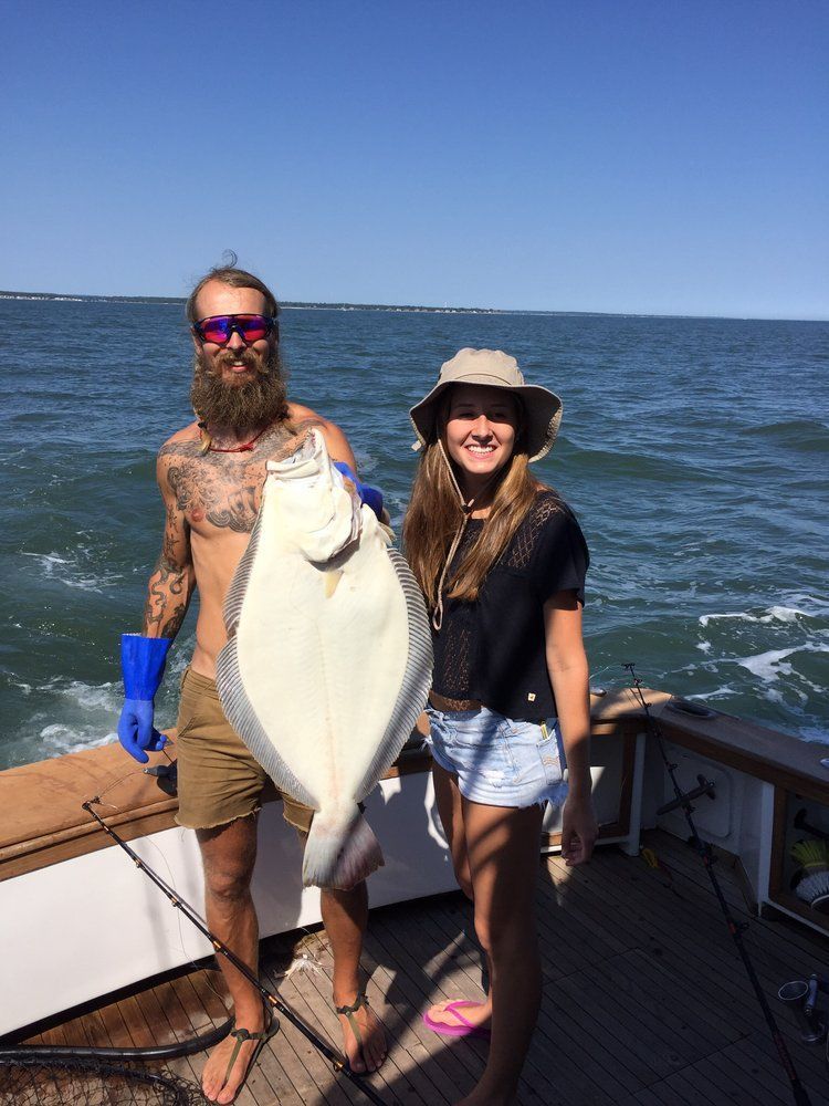 Two people on a boat holding a large fish, with ocean and blue sky behind them.