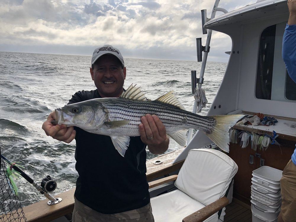 Man holding a large striped fish on a boat at sea, with choppy water and cloudy sky behind him