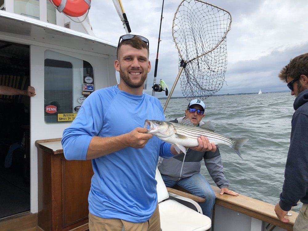 Man on a boat smiling and holding a fish, with another person and a fishing net in the background.