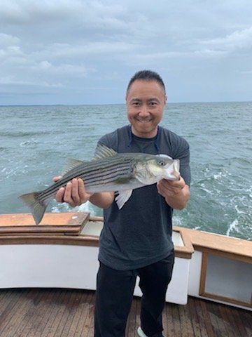 Man smiling on a boat holding a large striped fish with the ocean behind him
