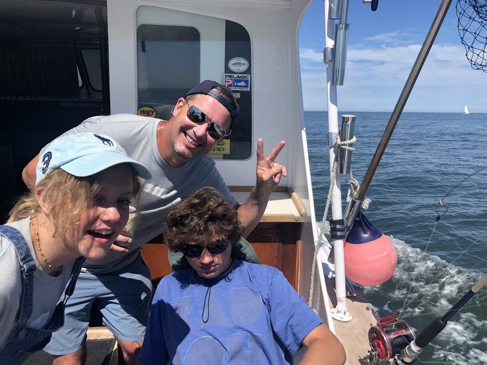 Three people smiling on a boat deck with open ocean in the background
