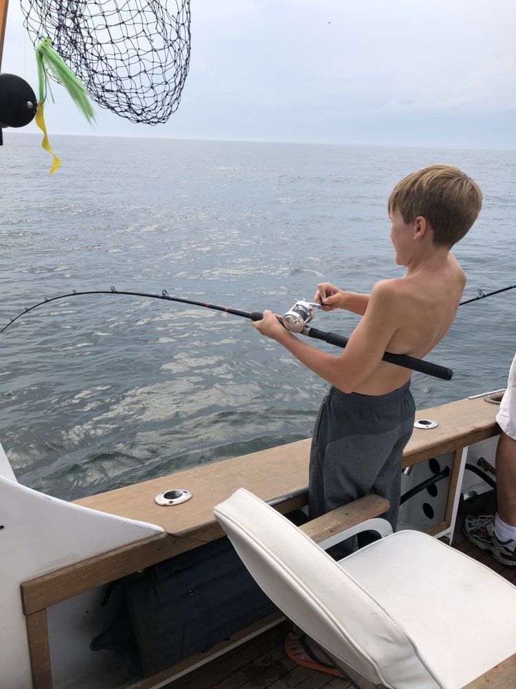Boy fishing off a boat deck beside calm open water, holding a bent fishing rod
